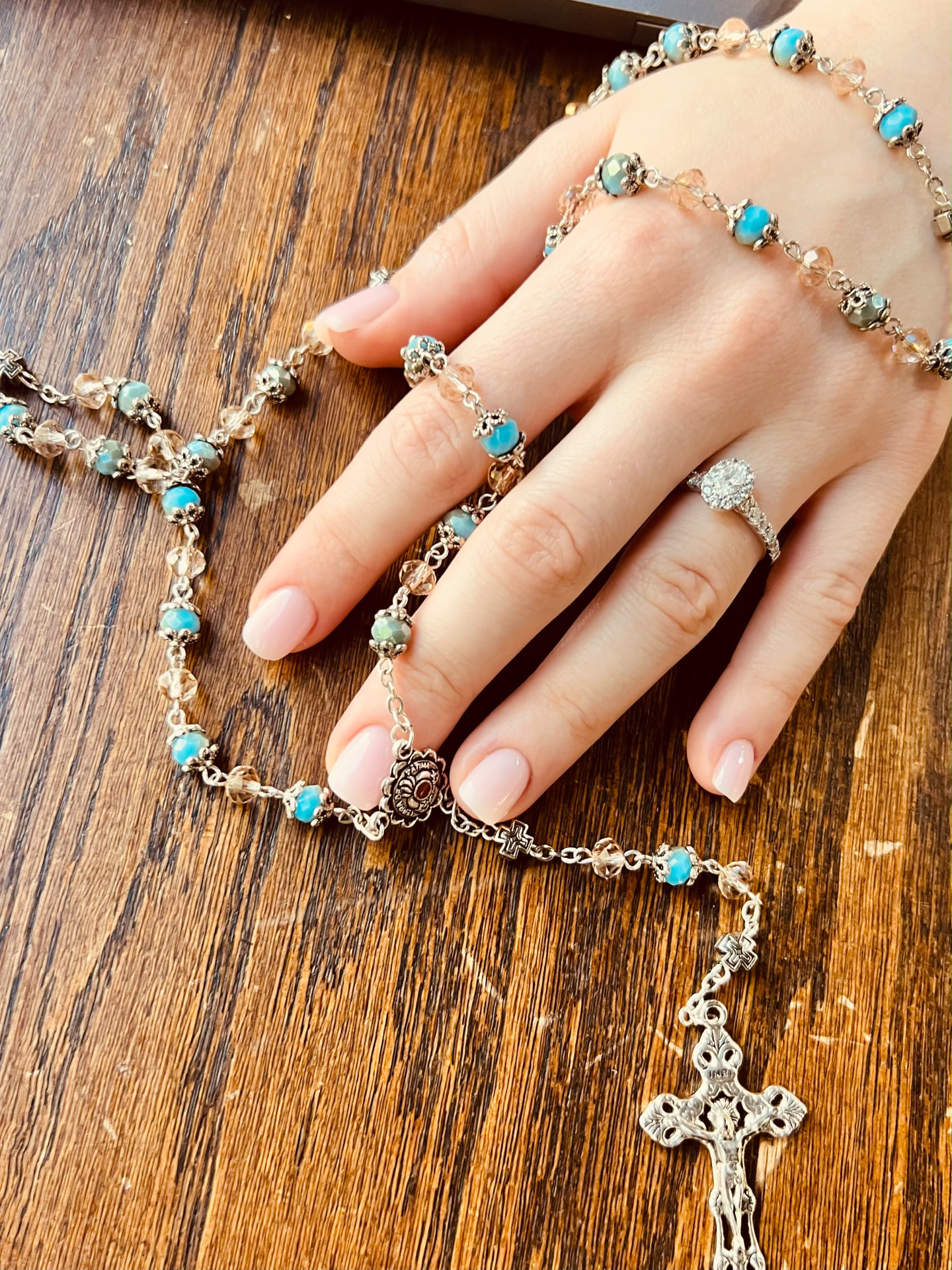 Mão pousada sobre uma mesa de madeira com um terço de contas azuis e um crucifixo de prata